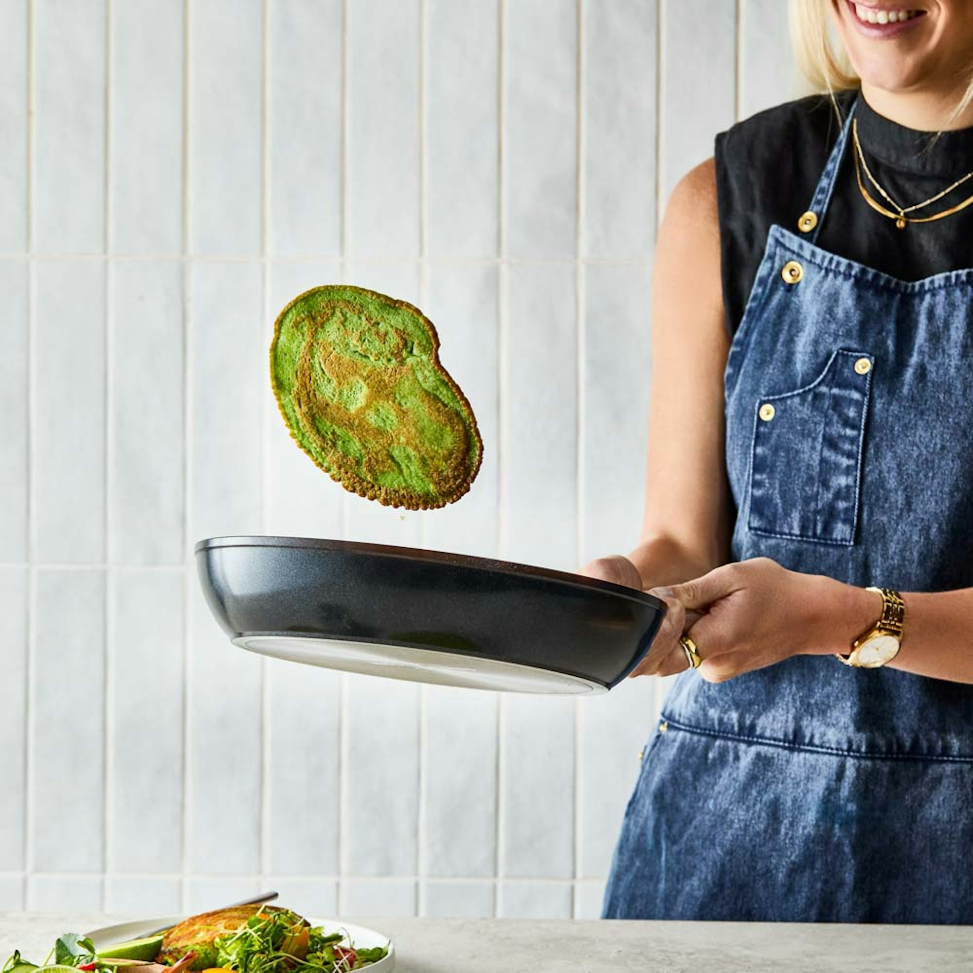 How to start cooking at home blog. Woman flipping green pancake in frypan.